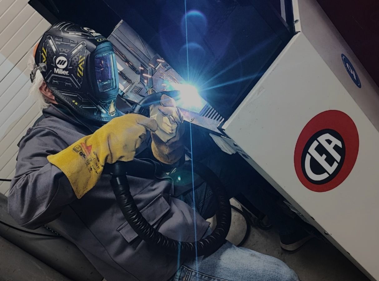 Schweißer in Schutzkleidung, Funken fliegen beim Schweißvorgang in einer dunklen Werkstatt.