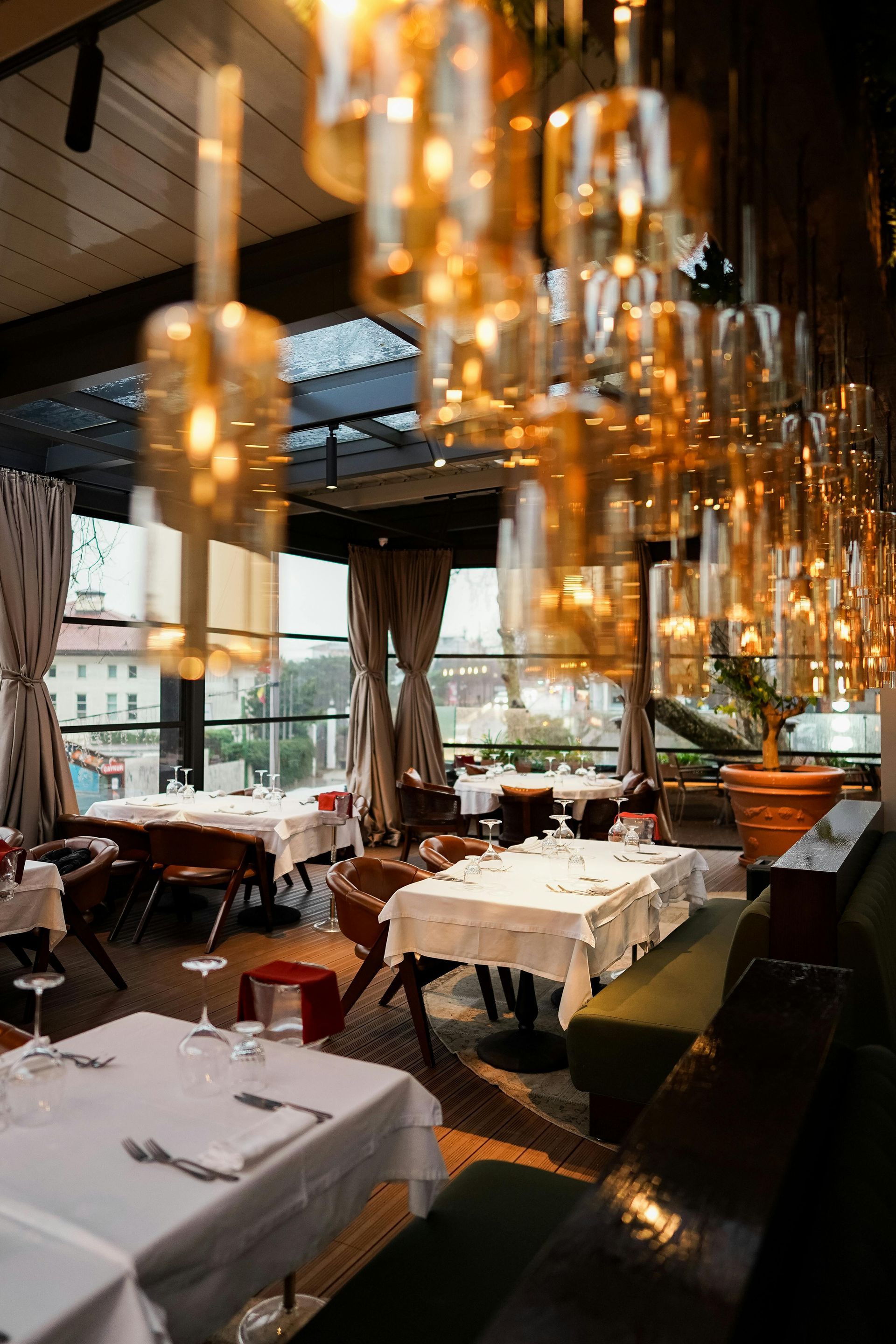 Elegante comedor de restaurante con manteles blancos, cálidas luces colgantes y grandes ventanales.