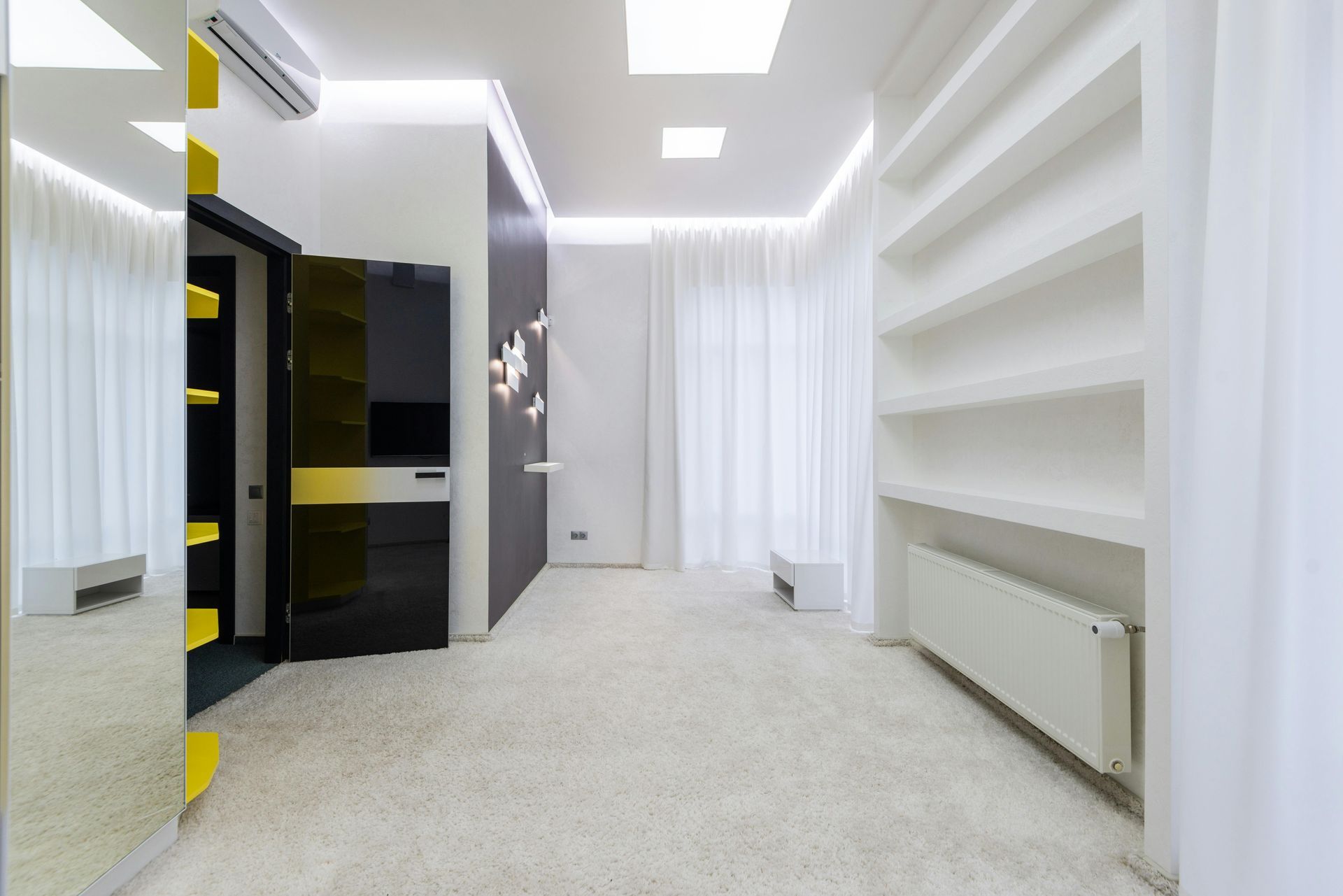 Vestidor moderno y luminoso con estantes blancos, moqueta gris y armarios de almacenamiento negros.