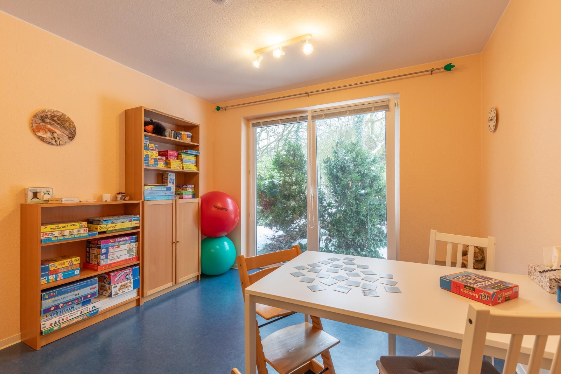 Helles Spielzimmer mit Spielzeug, Regalen, einem Tisch, Stühlen und Glasschiebetüren zum Garten.