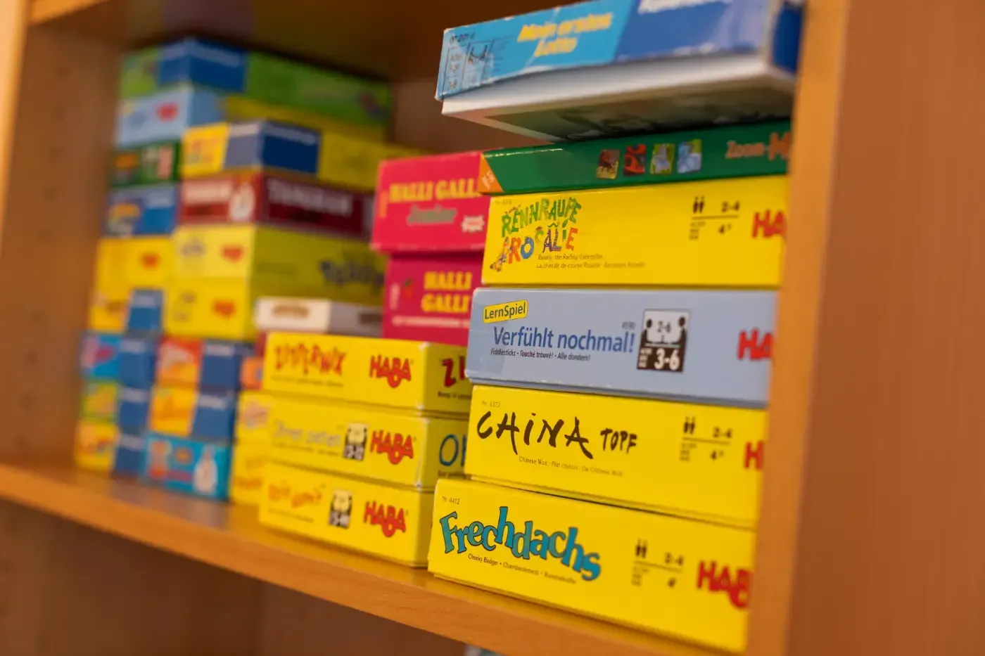 Auf einem Holzregal gestapelte bunte Brettspielkartons, wobei gelbe und blaue Kartons sichtbar sind.