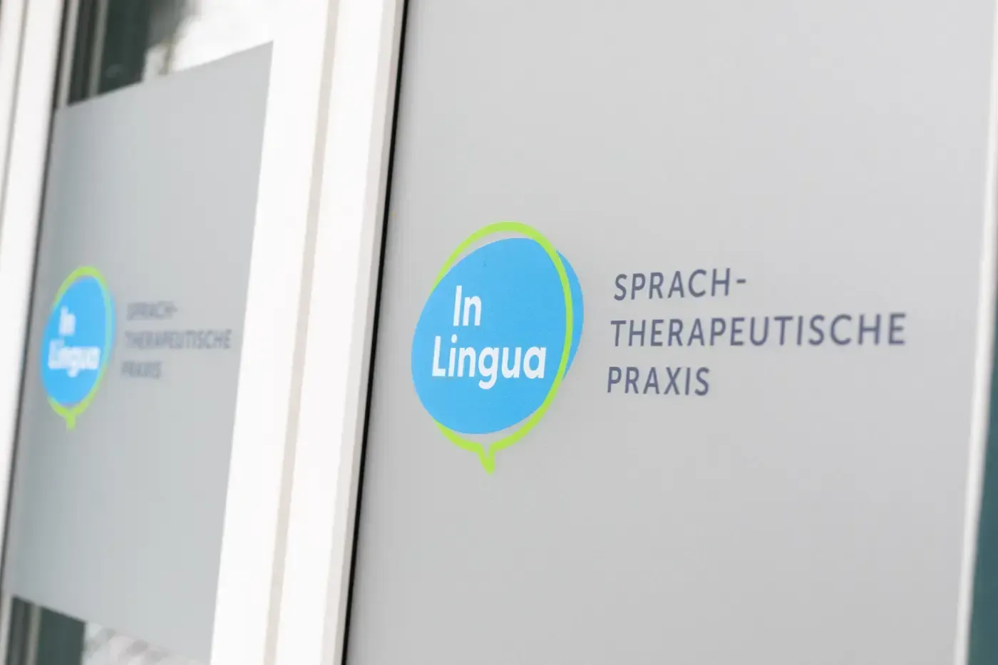Ein Schild mit der Aufschrift „In Lingua“ an der Milchglastür einer Sprachtherapiepraxis.