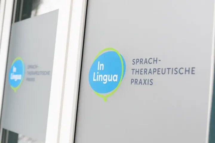 Ein Schild mit der Aufschrift „In Lingua“ an der Milchglastür einer Sprachtherapiepraxis.