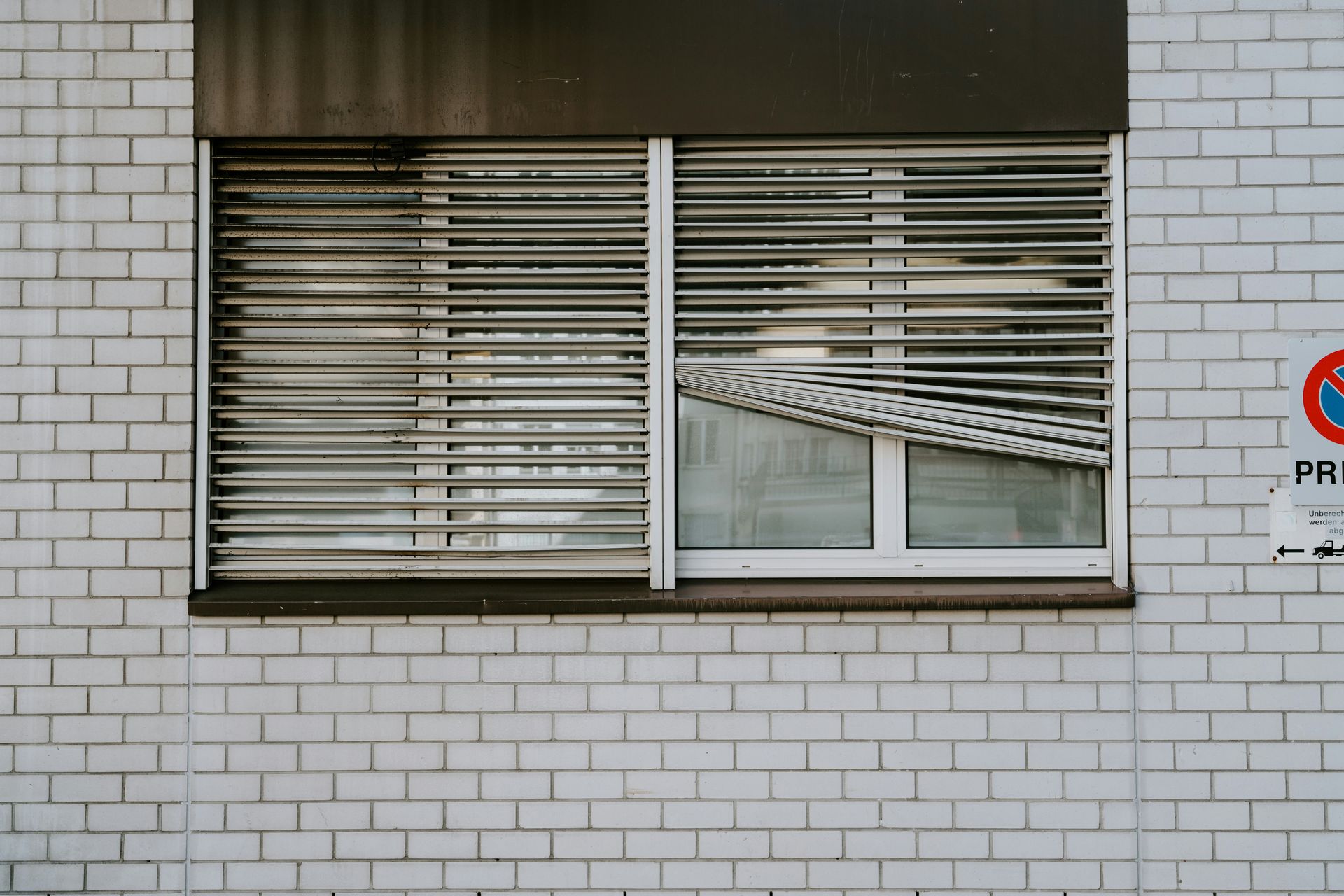 Ventana con persianas cerradas en un edificio de ladrillo blanco. Vista parcial del tejado visible a través de la sección abierta.