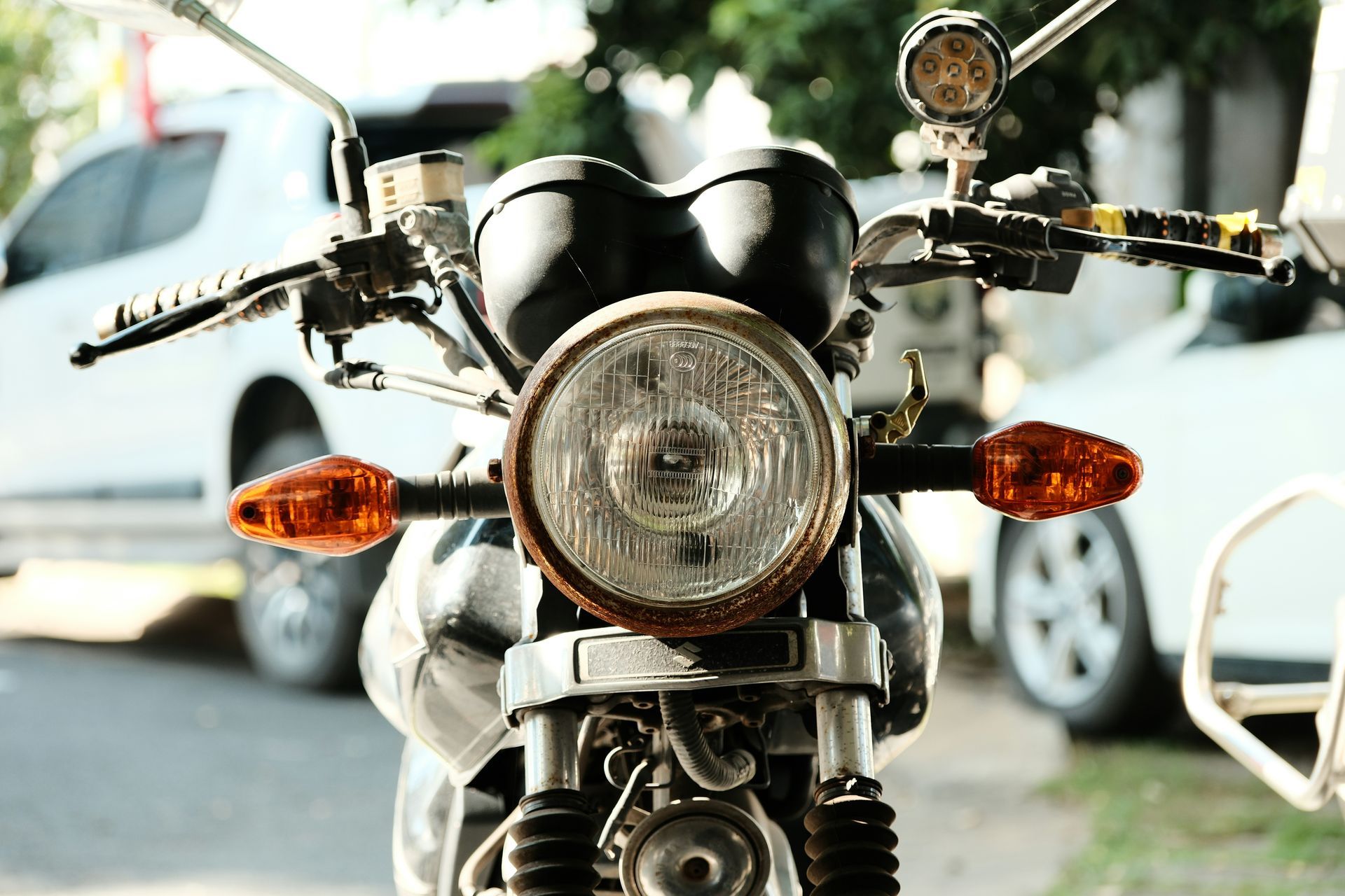 Primer plano del frontal de una motocicleta: faro redondo, intermitentes naranjas, manillar cromado.