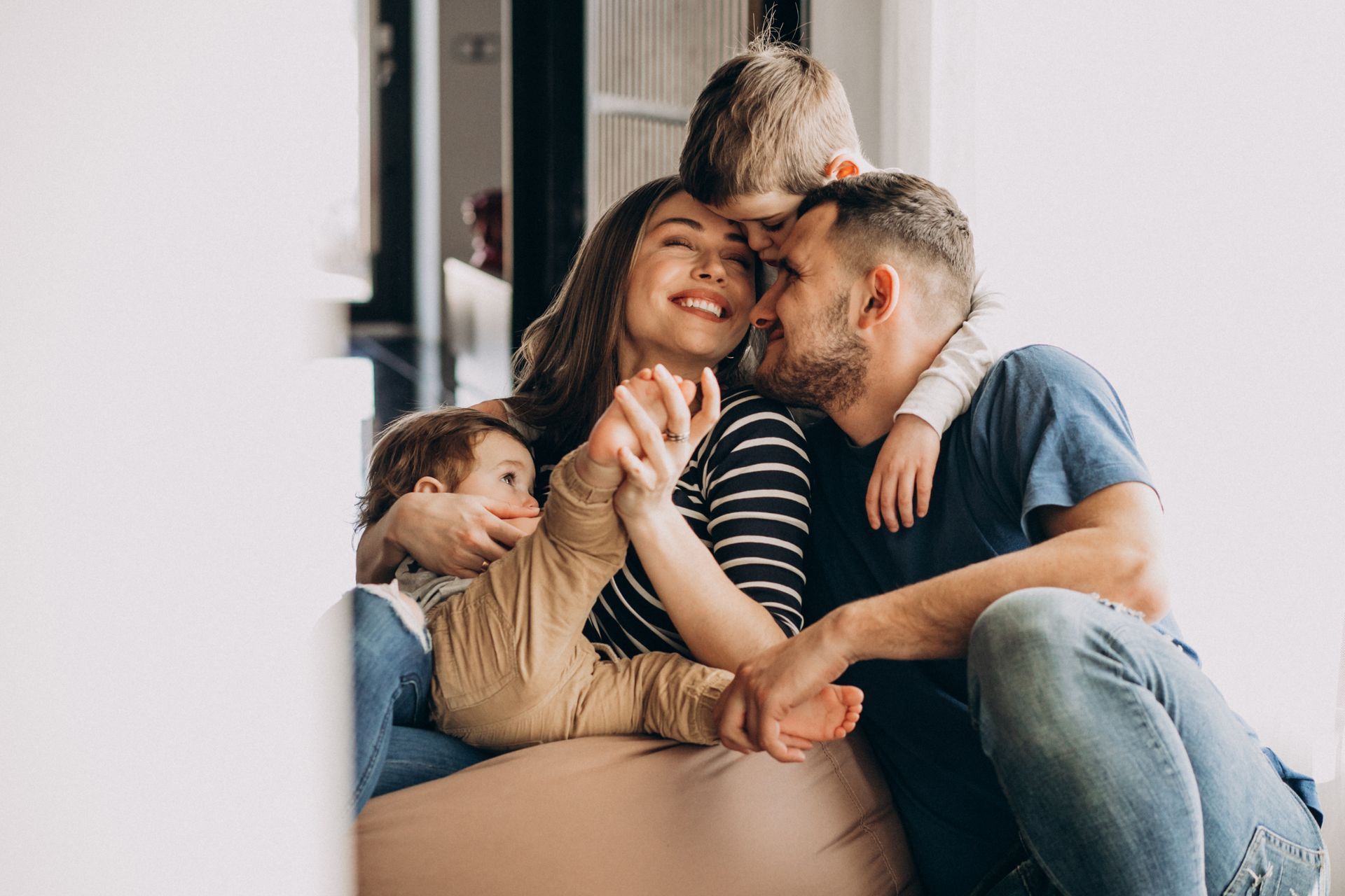 Una familia se abraza, sonriendo, en casa. Una madre, un padre y dos hijos.