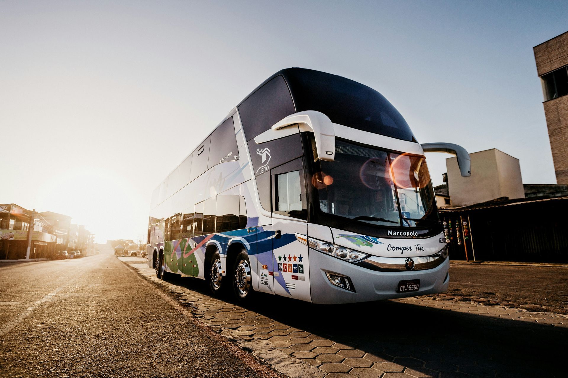 Autobús de dos pisos en la calle, reflejando la luz del sol. Blanco y azul con gráficos coloridos.