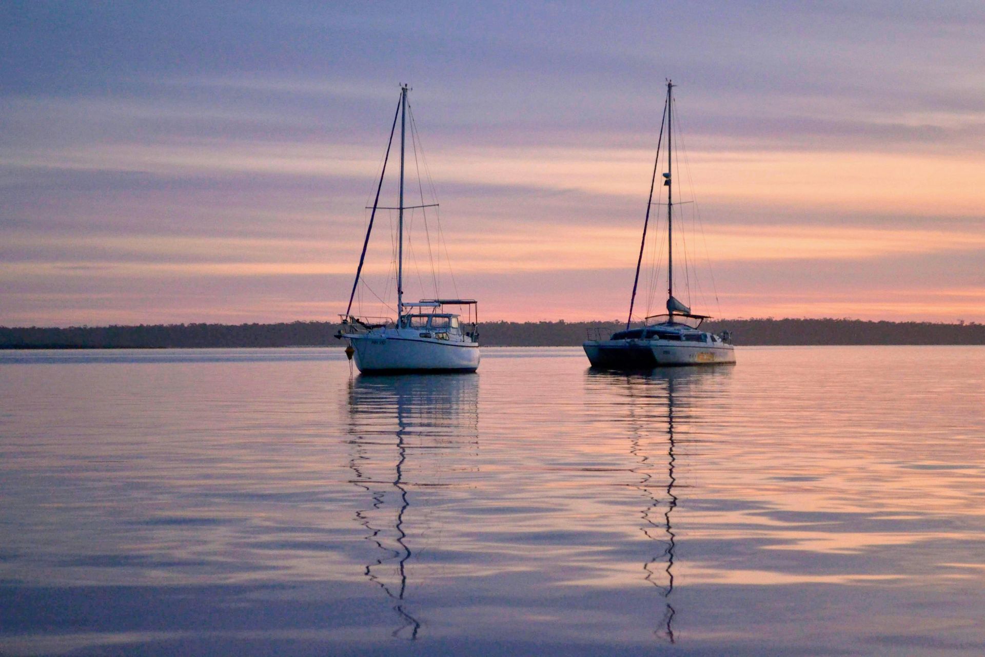 Dos veleros en aguas tranquilas al atardecer, reflejando el cielo colorido.