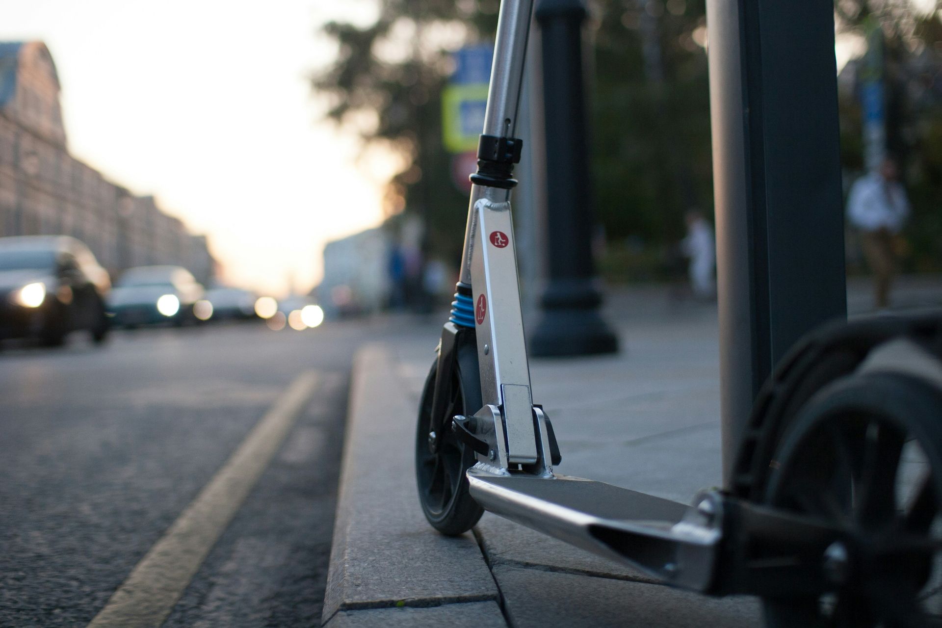 Patinete eléctrico aparcado en una acera junto a un bordillo y una calle con coches.