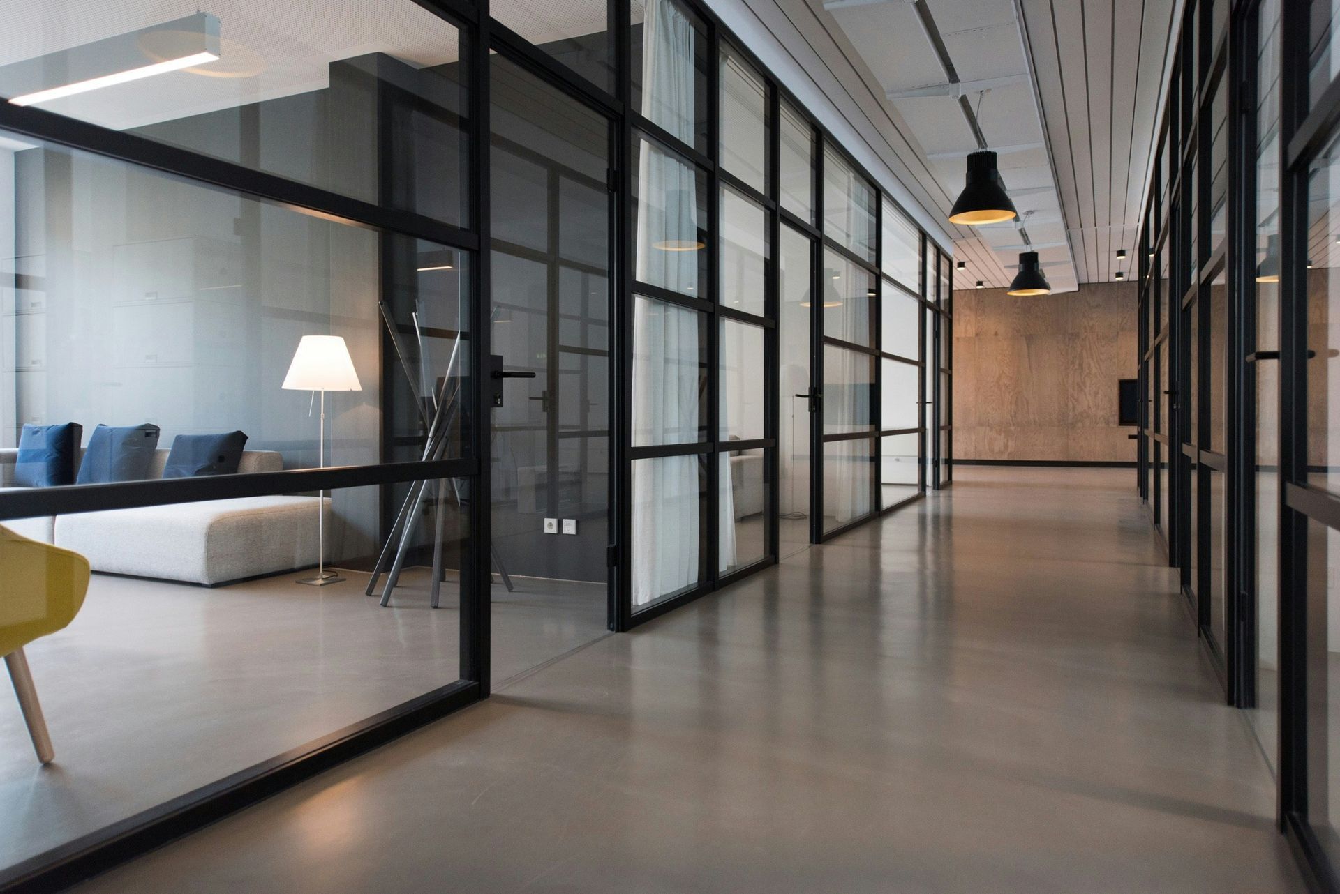 Pasillo de oficina moderno con habitaciones con paredes de vidrio y pisos y paredes grises.