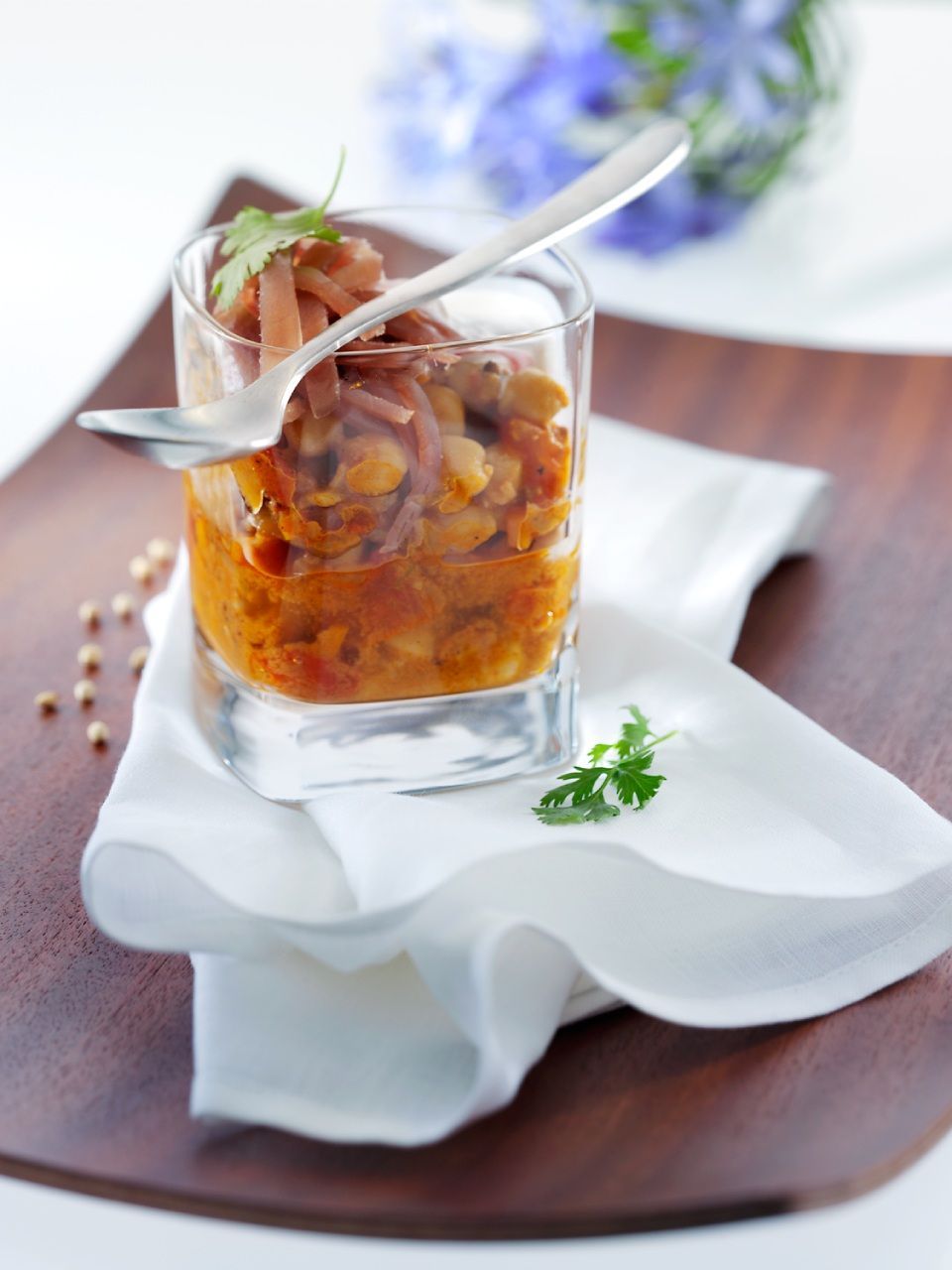 Vorspeise im Glas: Bohnen, Gemüse und Wurstwaren, mit Löffel. Serviert auf einer weissen Serviette und einem Holztablett.