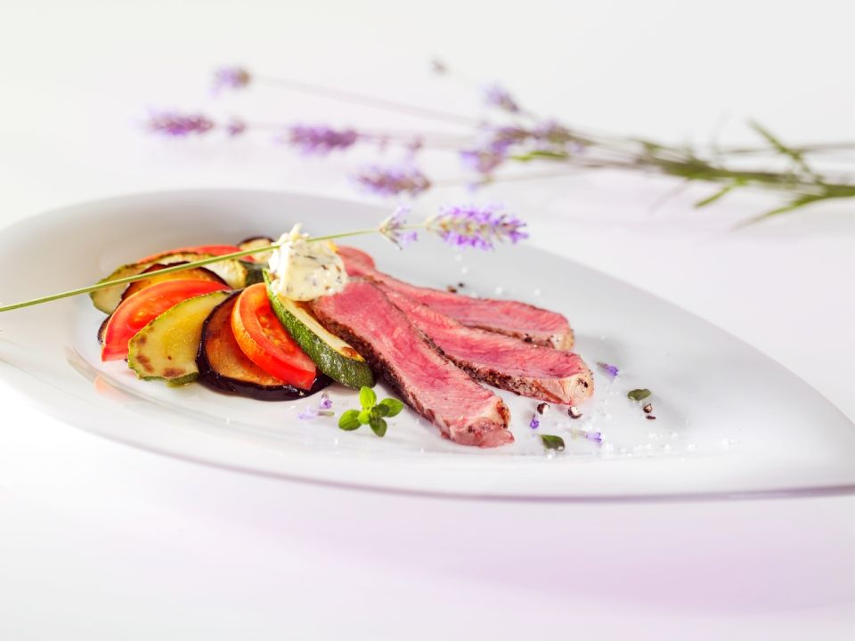 Gekochtes Fleisch in Scheiben und gegrilltes Gemüse auf einem weissen Teller, garniert mit Lavendel.