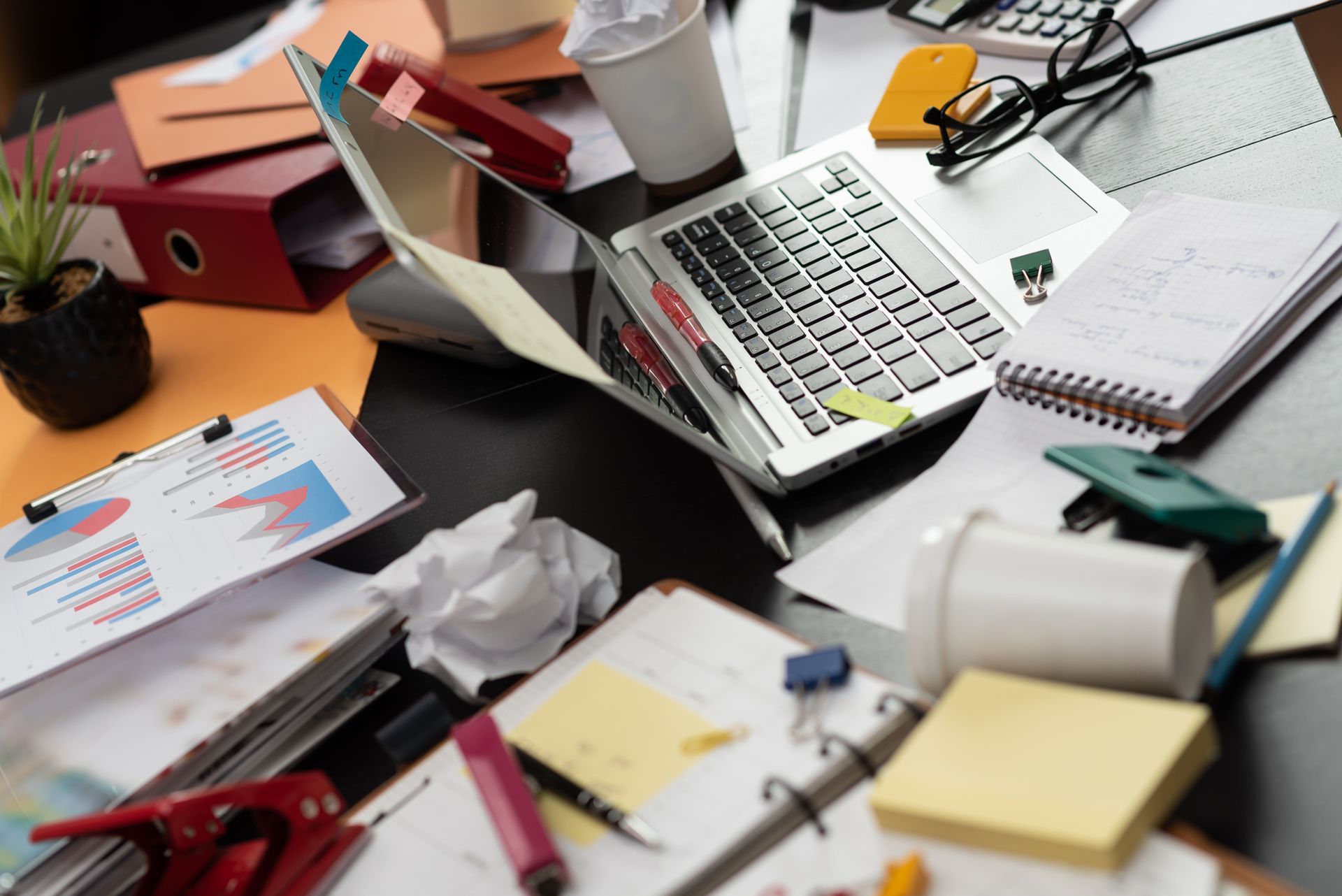 Bureau encombré d'un ordinateur portable, de papiers, de fournitures de bureau.
