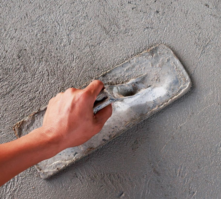 Personne tenant une truelle et lissant du béton frais.