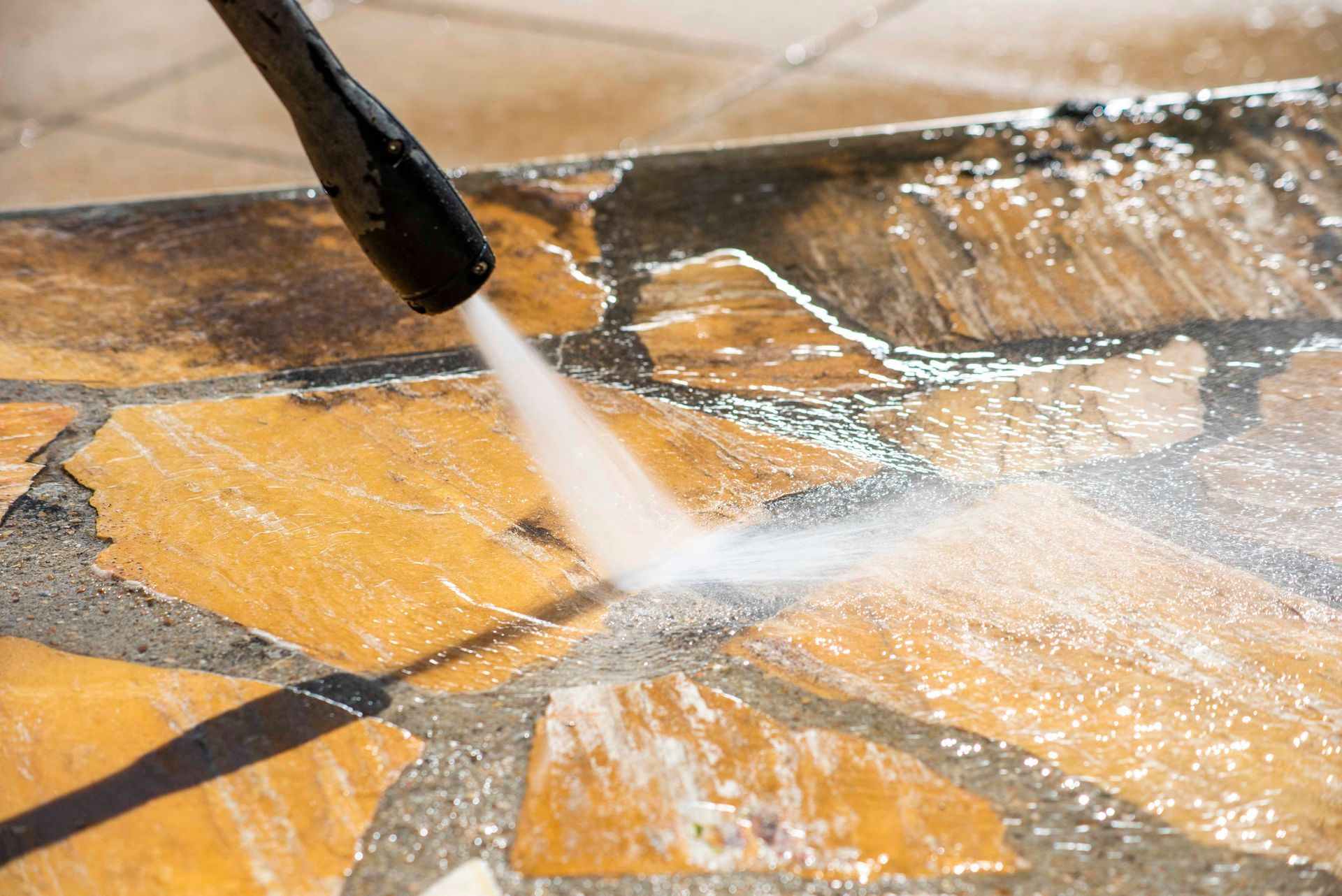 Un nettoyeur haute pression projette de l'eau sur une terrasse en pierre.