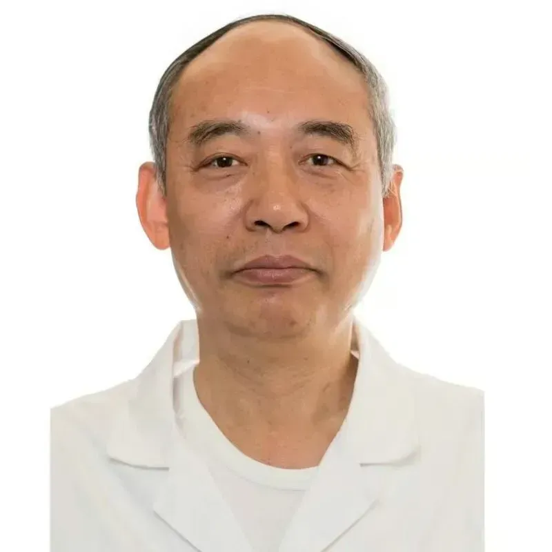 Mann mit dunklem Haar, trägt einen weißen Kittel, blickt nach vorne, neutraler Gesichtsausdruck.