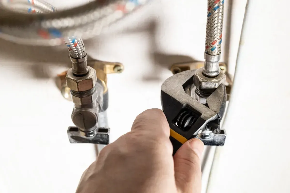 Mano que utiliza una llave para apretar un accesorio en una tubería de plomería.