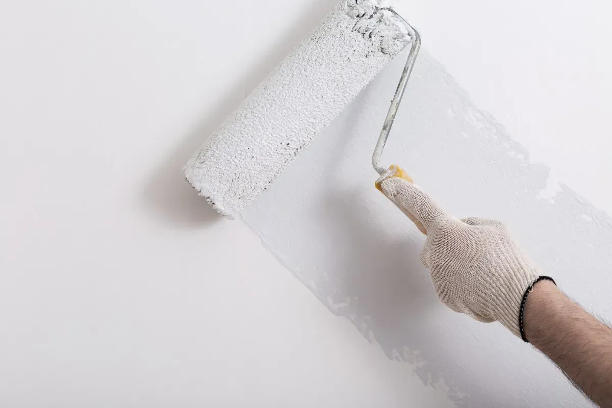 Persona que lleva un guante pintando una pared blanca con un rodillo de pintura.