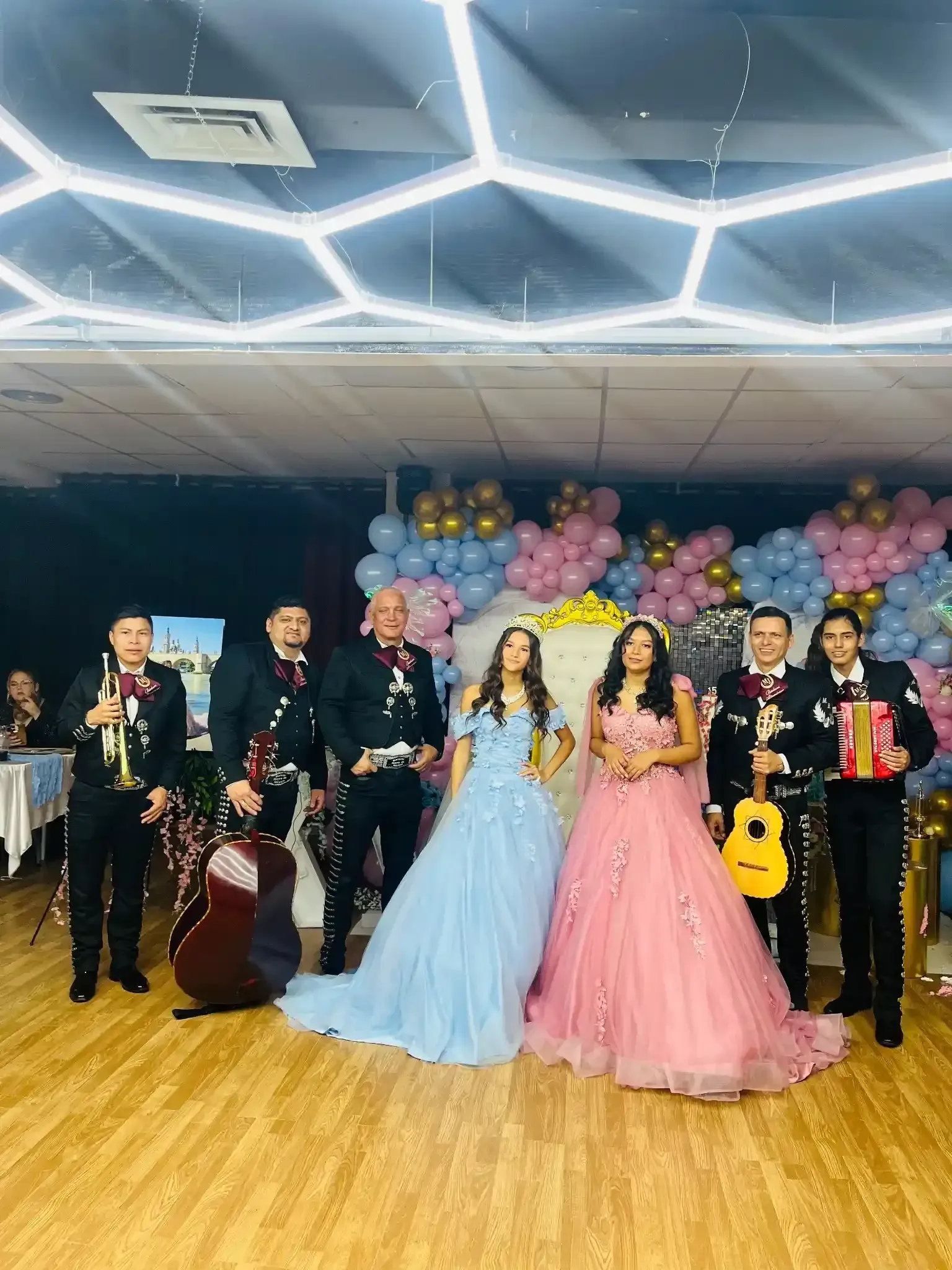 Banda de mariachis con dos mujeres con vestidos formales en una fiesta, probablemente una quinceañera.