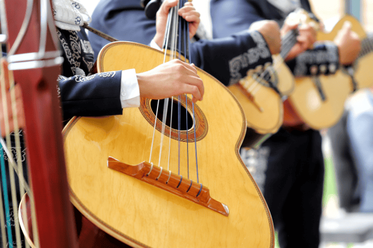 Músico mariachi tocando una guitarra, parte de una banda con vestimenta formal.