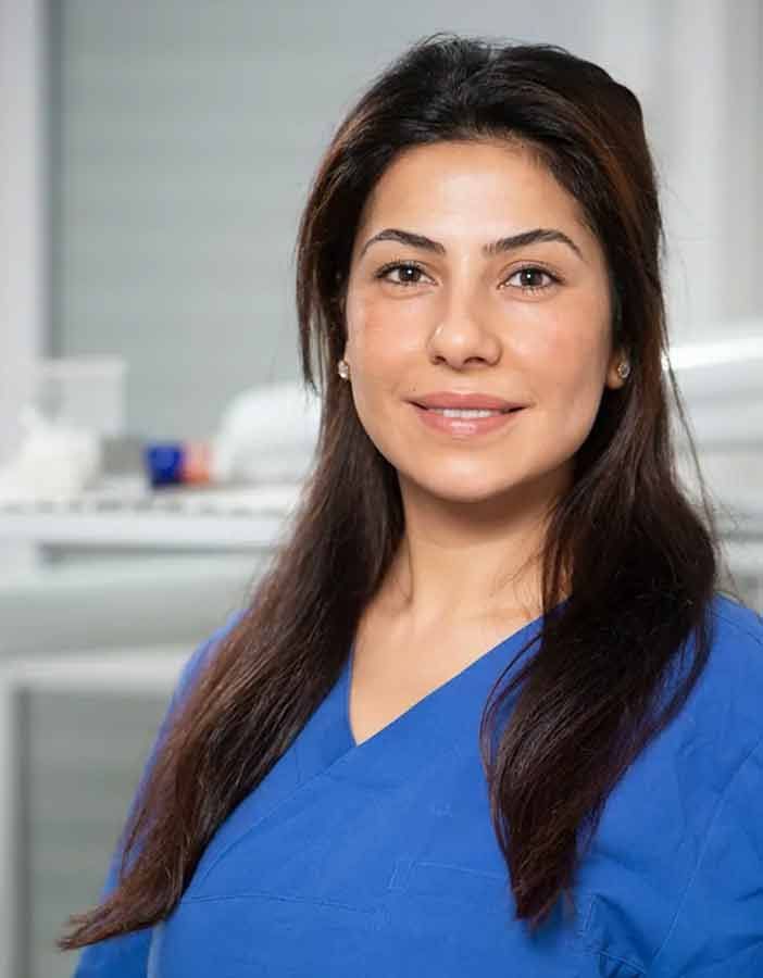 Eine Frau in einem blauen OP-Kittel lächelt in die Kamera.