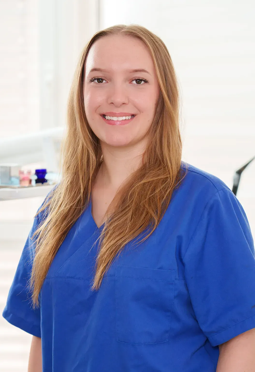 Frau im blauen OP-Kittel lächelt, möglicherweise in einer Zahnarztpraxis.