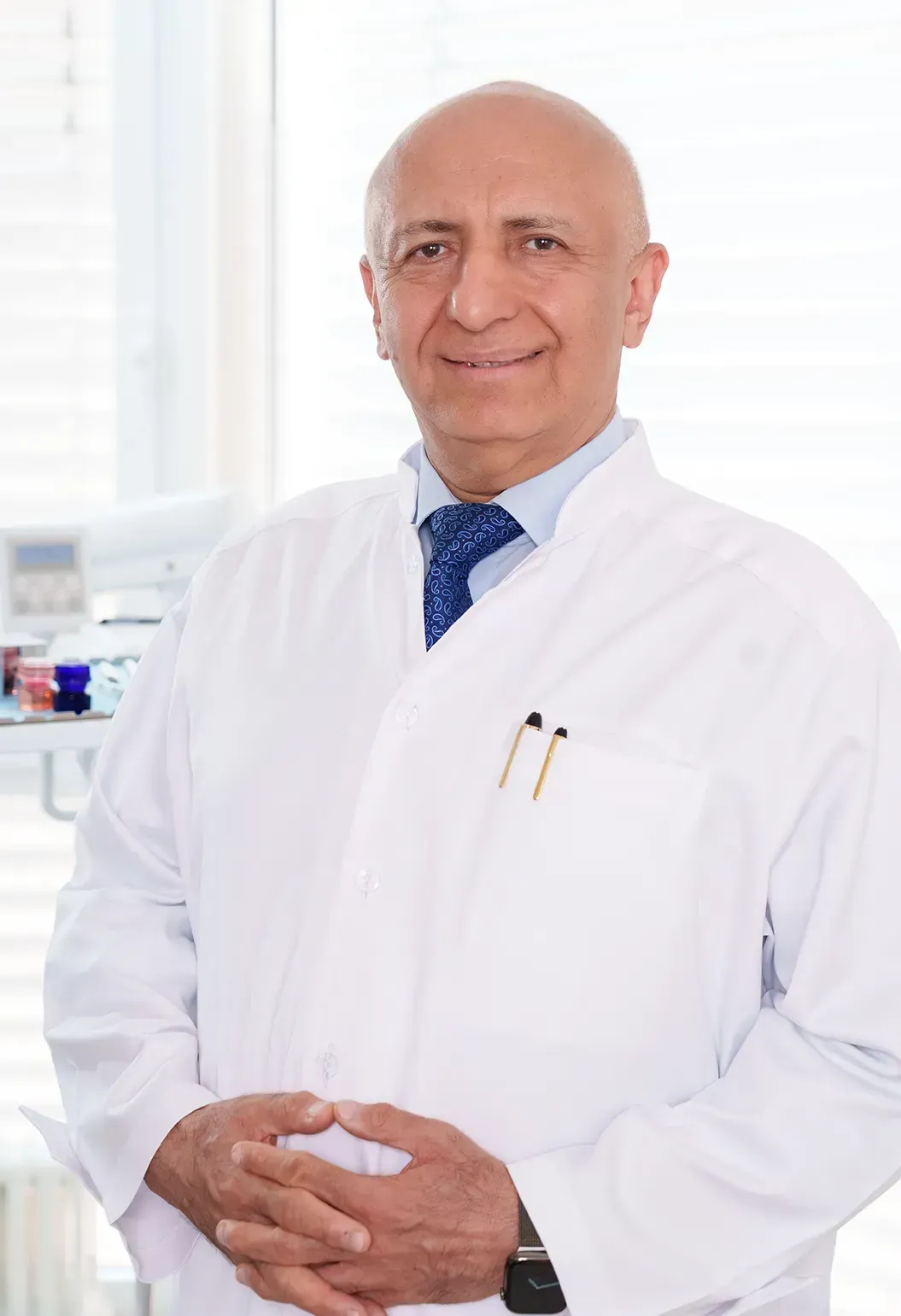 Ein kahlköpfiger Mann in weißem Kittel und Krawatte lächelt in die Kamera.