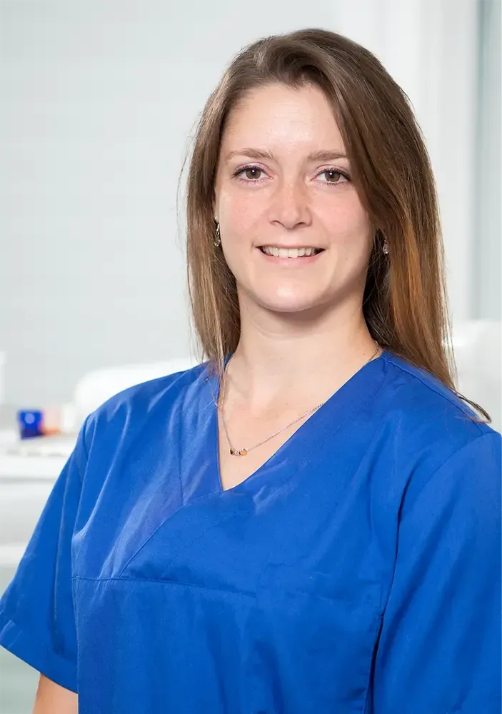 Frau im blauen OP-Kittel lächelt; sanfte Beleuchtung in einem medizinischen Umfeld.