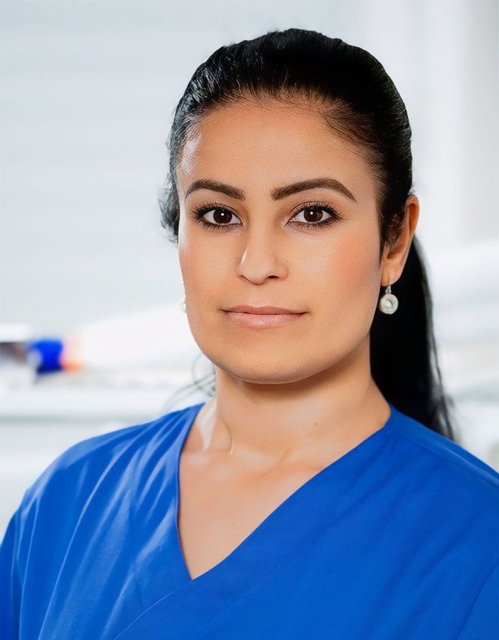 Eine Frau trägt einen blauen OP-Kittel und Ohrringe.