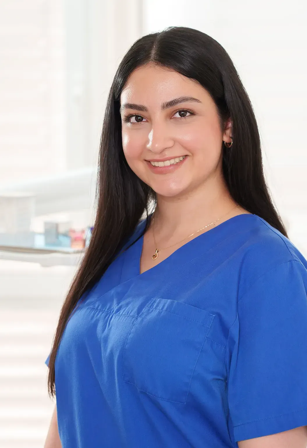 Frau im blauen OP-Kittel lächelt in einer hellen medizinischen Umgebung in die Kamera.