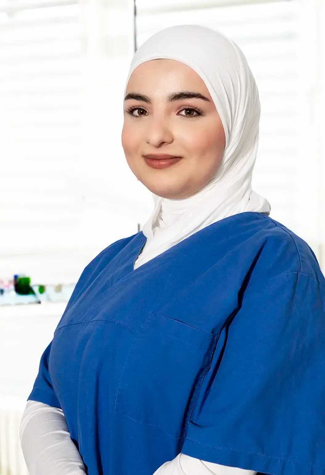 Frau im blauen OP-Kittel lächelt, möglicherweise in einer Zahnarztpraxis.