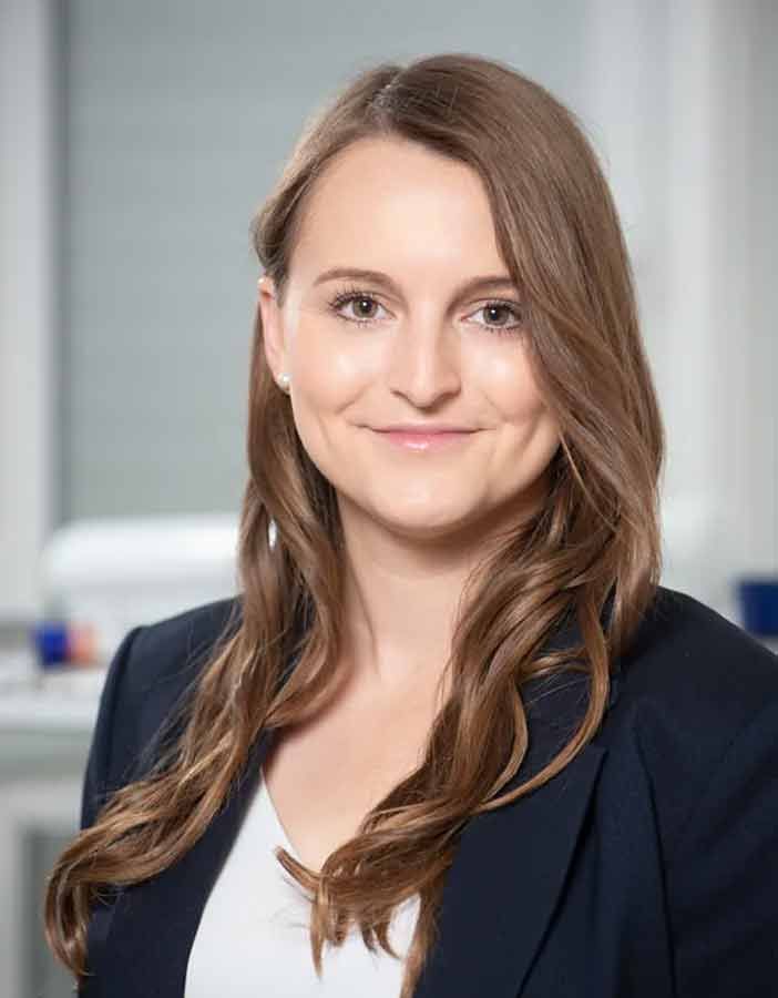 Eine Frau in einer blauen Jacke und einem weißen Hemd lächelt in die Kamera.