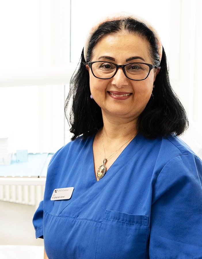 Eine Frau im blauen OP-Kittel lächelt in die Kamera.