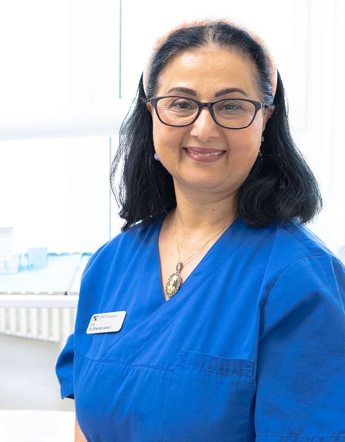 Eine Frau im blauen OP-Kittel lächelt in die Kamera.