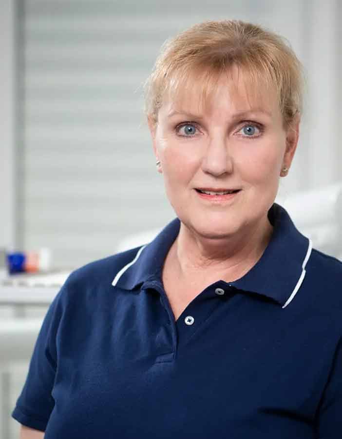 Eine Frau trägt ein blaues Poloshirt und lächelt in die Kamera.