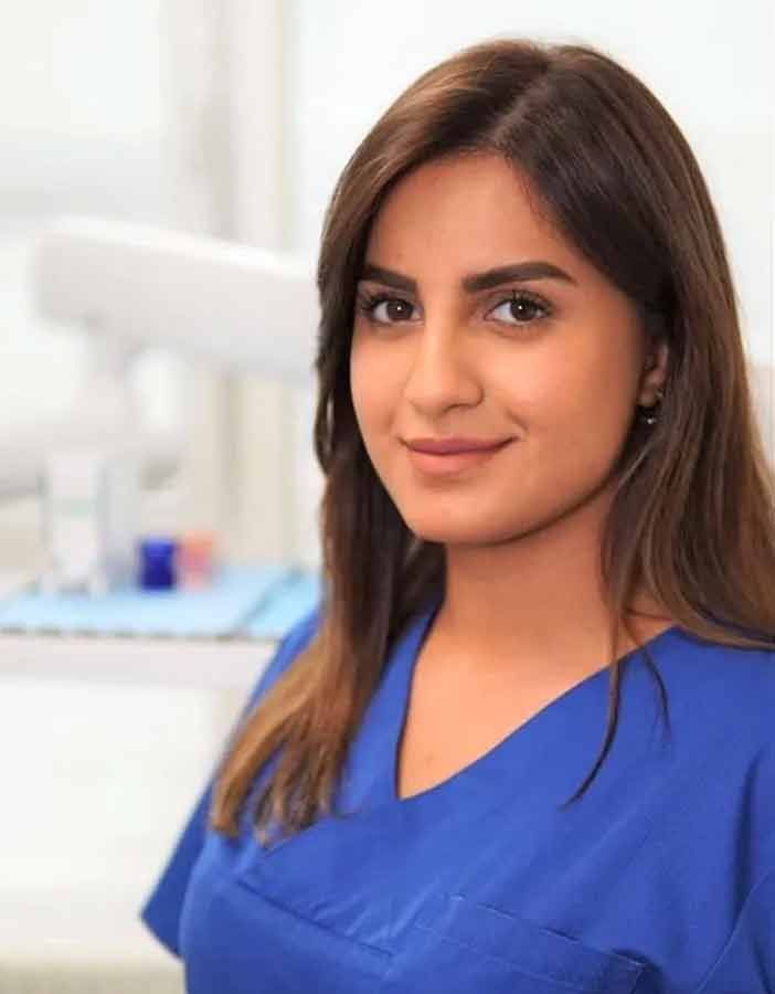 Eine Frau im blauen OP-Kittel lächelt in einer Zahnarztpraxis in die Kamera.