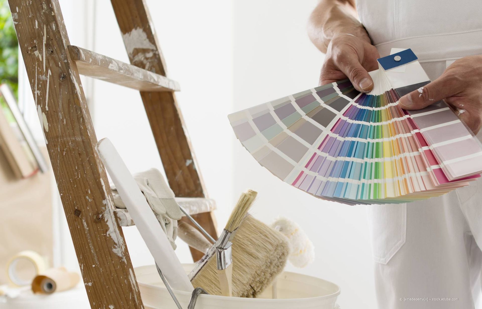 Eine Person hält einen Farbfächer in der Nähe einer Leiter, Pinseln und eines Eimers.