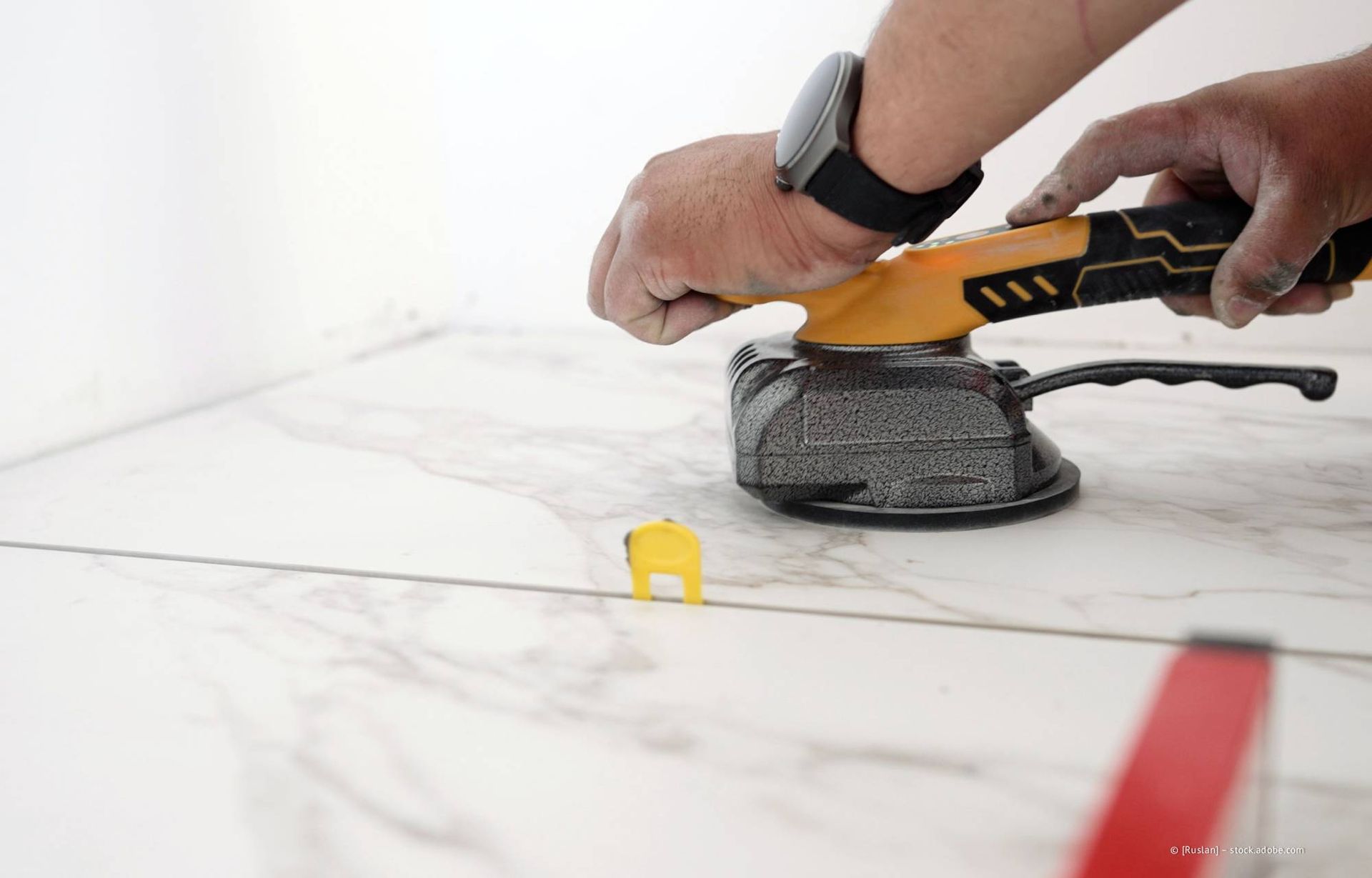 Person, die mit einem Elektrowerkzeug Fliesenböden glättet.