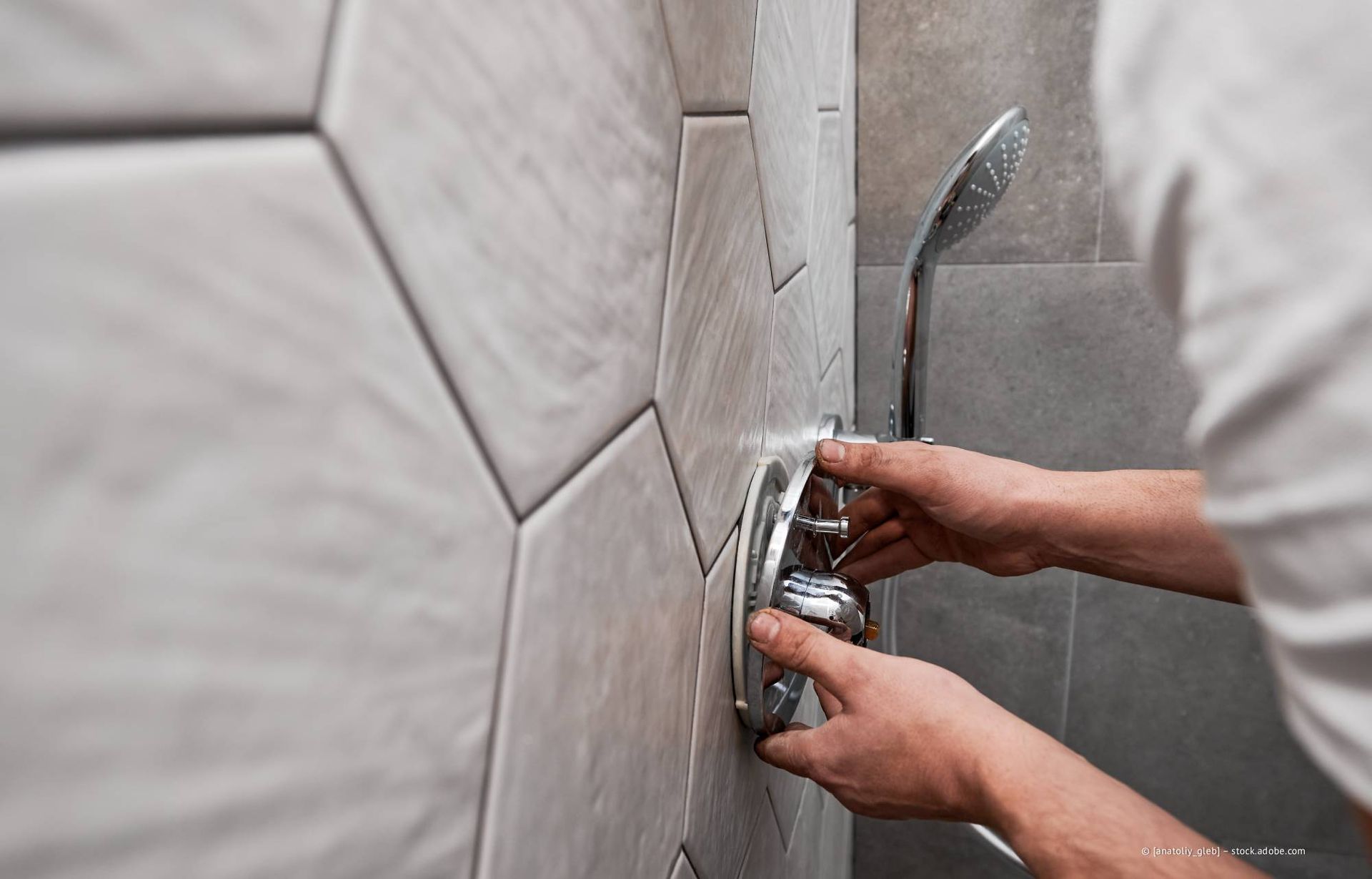 Eine Person montiert eine Duscharmatur an einer grauen Fliesenwand.
