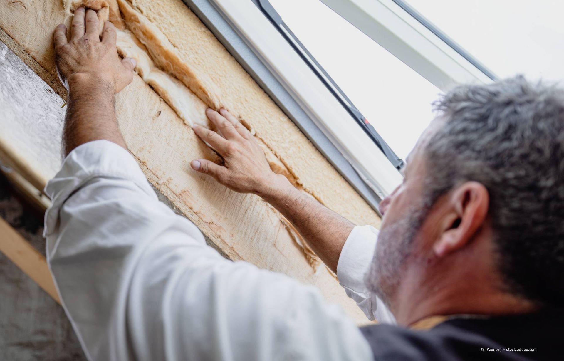 Eine Person installiert Dämmmaterial um einen Fensterrahmen herum.
