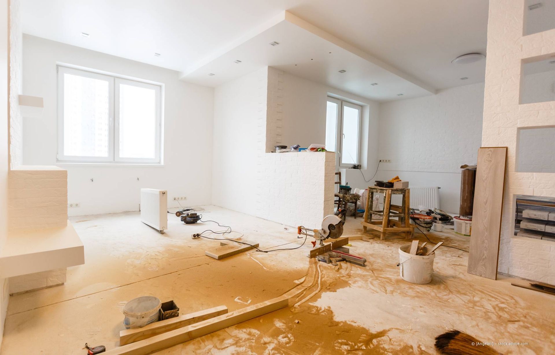 Zimmer im Umbau, weiße Wände und Boden, Bauschutt, zwei Fenster.