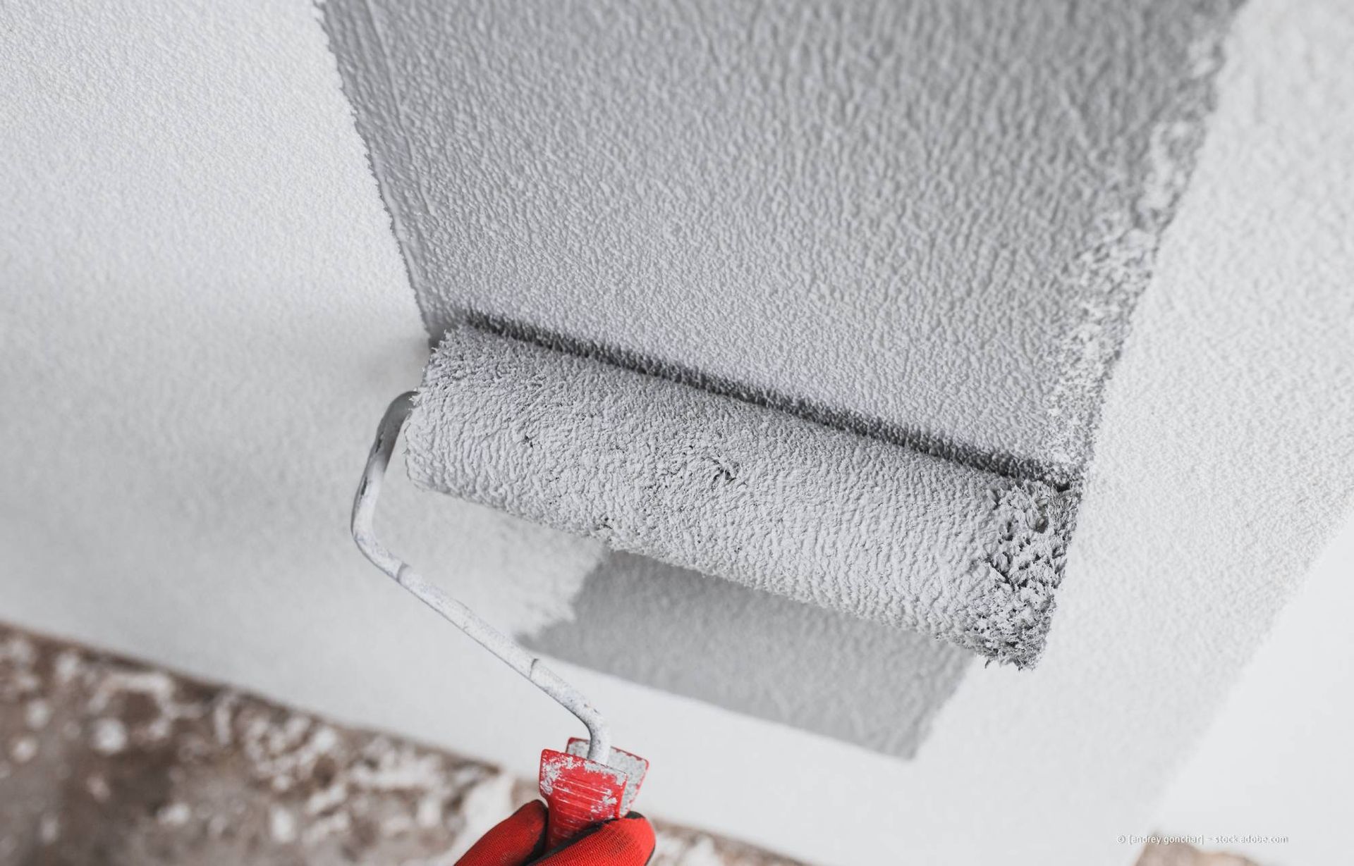 Eine Farbrolle trägt graue Farbe auf eine weiße Decke auf.