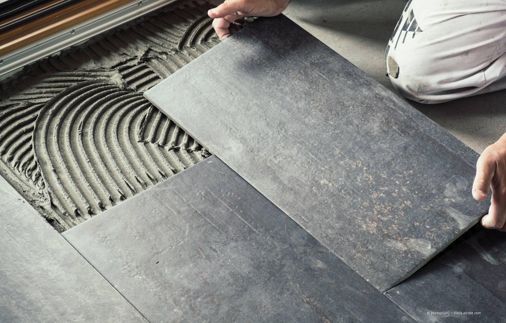 Eine Person legt eine graue Fliese auf Mörtel auf einem Fußboden.