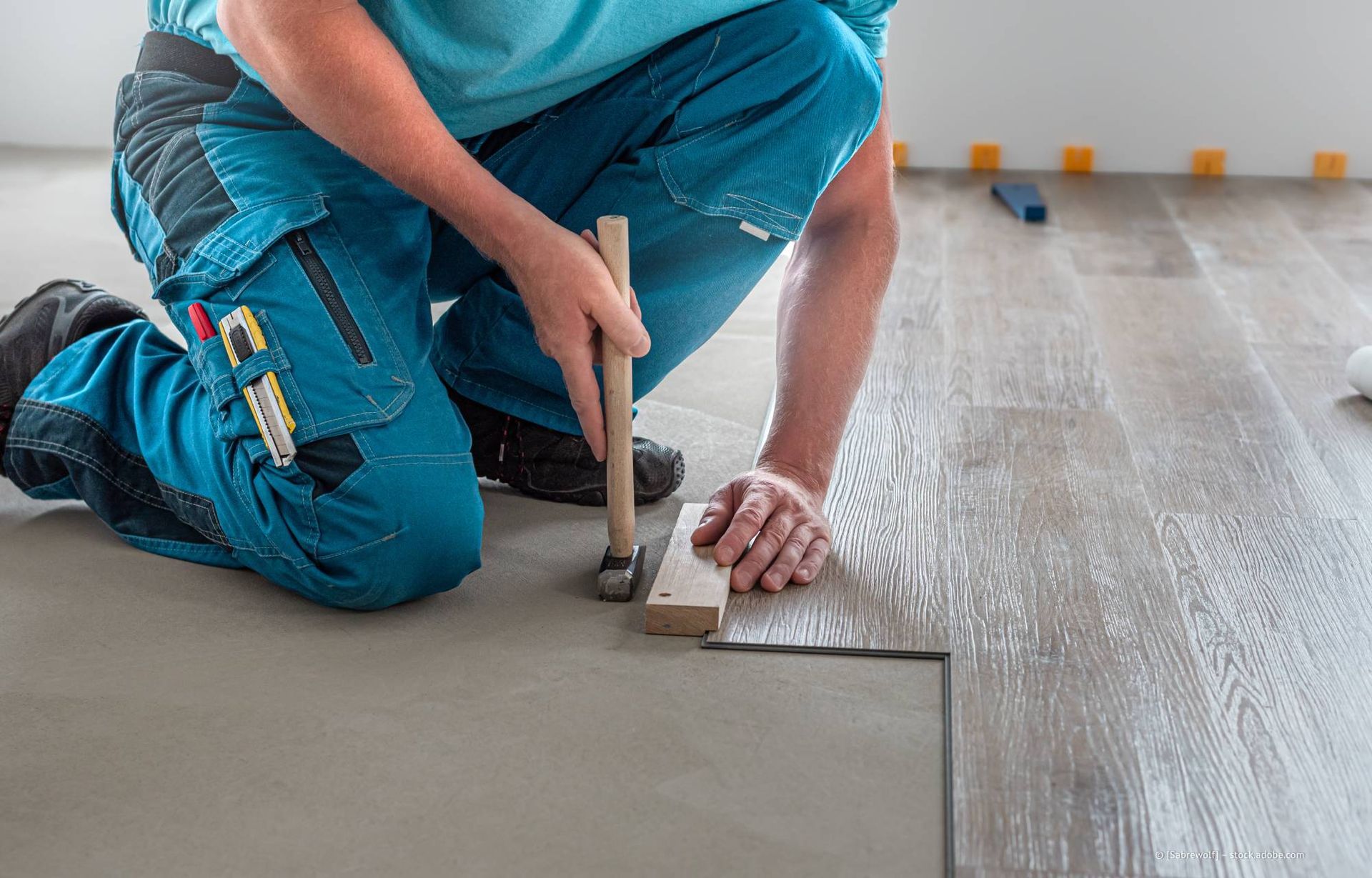 Eine Person verlegt mit Hammer und Klotz einen Bodenbelag in Holzoptik.
