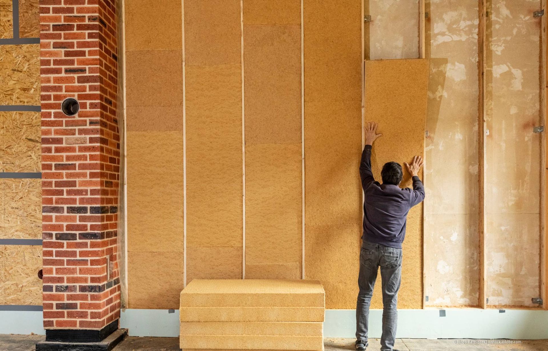 Eine Person montiert Korkdämmplatten an einer Wand mit Holzständerwerk in der Nähe eines gemauerten Pfeilers.