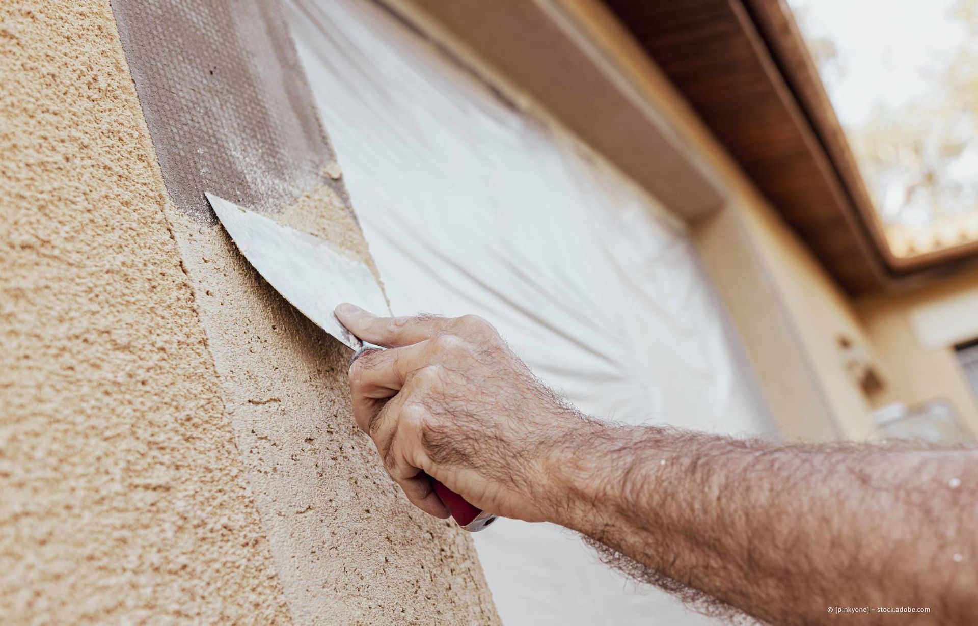 Eine Person trägt mit einem Spachtel Stuck auf eine Wand auf.