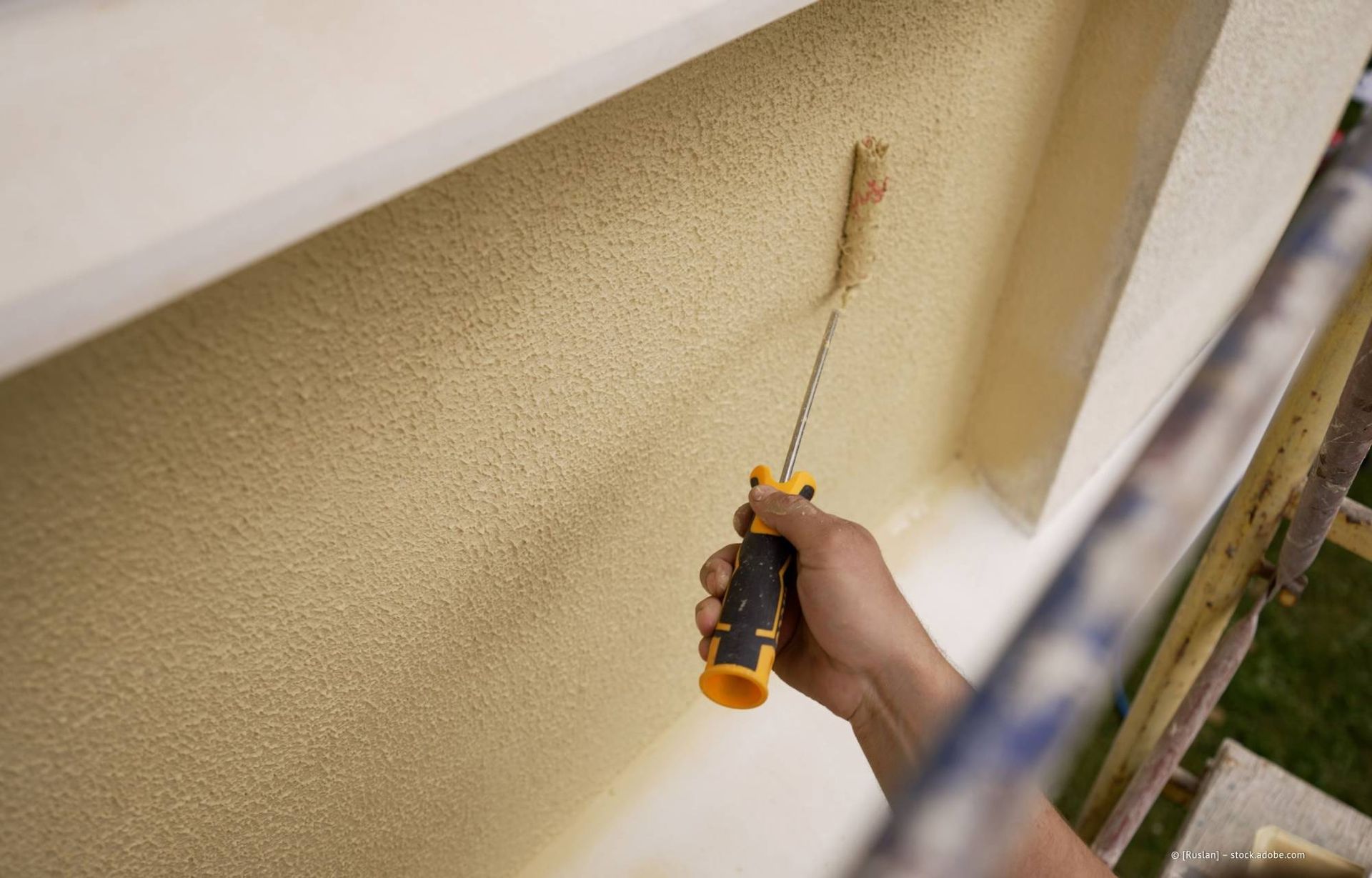 Die strukturierte Außenwand wurde in der Nähe eines weißen Fensterrahmens von Hand mit einer Farbrolle gestrichen.