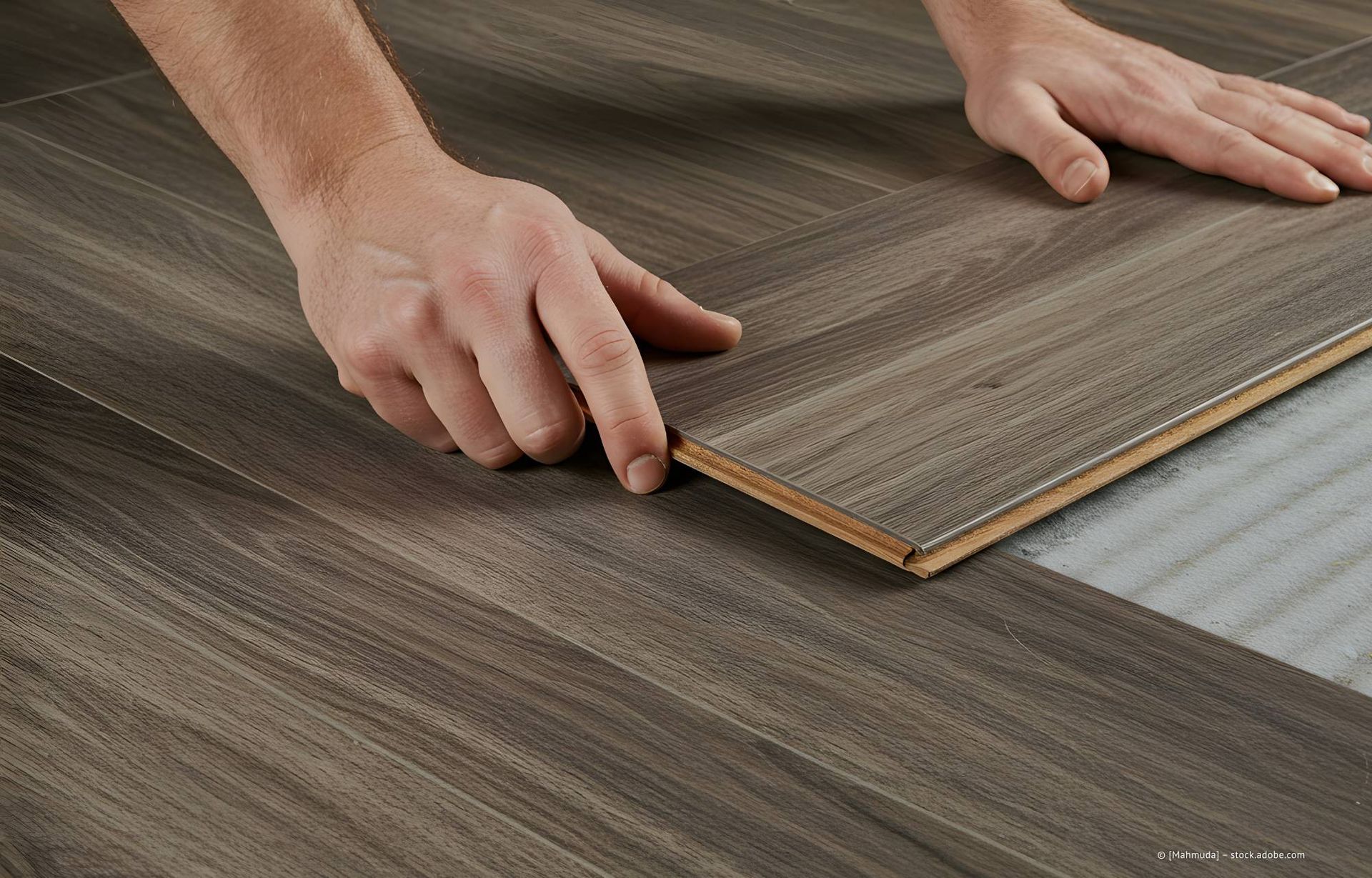 Hände verlegen Fußböden in Holzoptik und richten die Kanten aus.