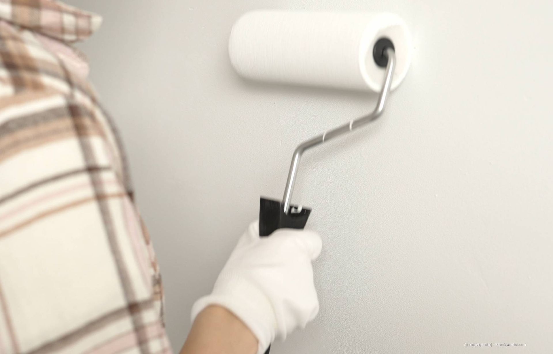 Eine Person mit Handschuhen streicht eine Wand mit einer Farbrolle.