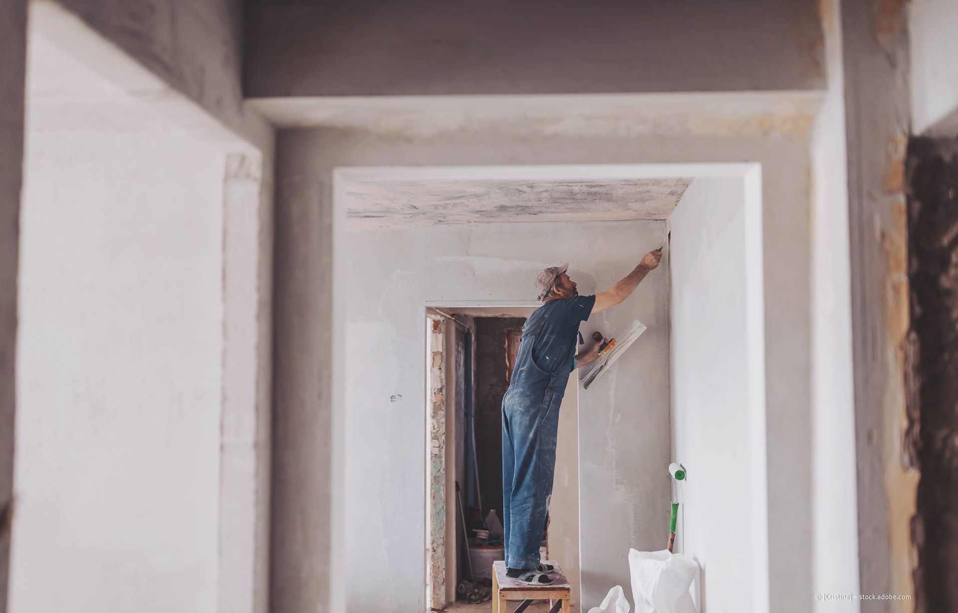 Ein Mann auf einem Hocker verputzt eine Wand in einem im Bau befindlichen Raum.